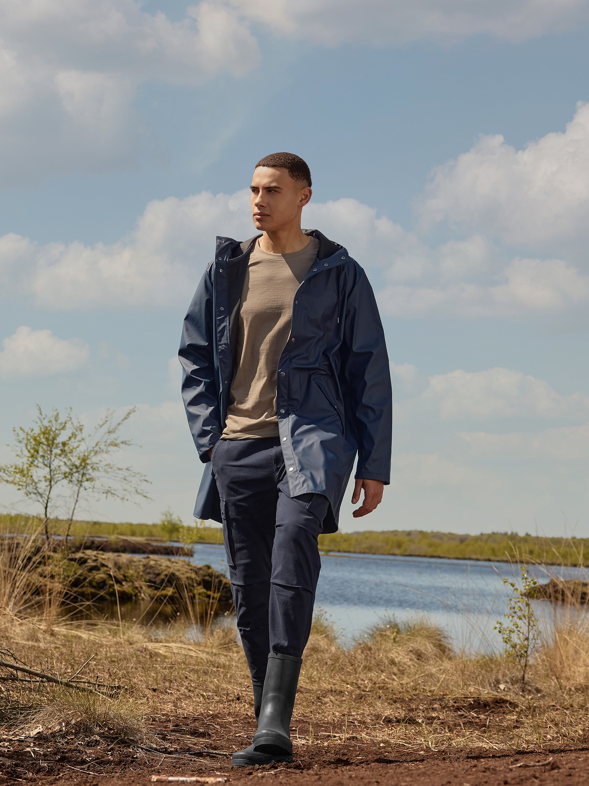 Imperméable et pantalon bleu marine pour homme, t-shirt marron, bottes en caoutchouc noires dans la nature.