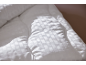Couette blanche avec motif texturé, éclairée par la lumière et les ombres.