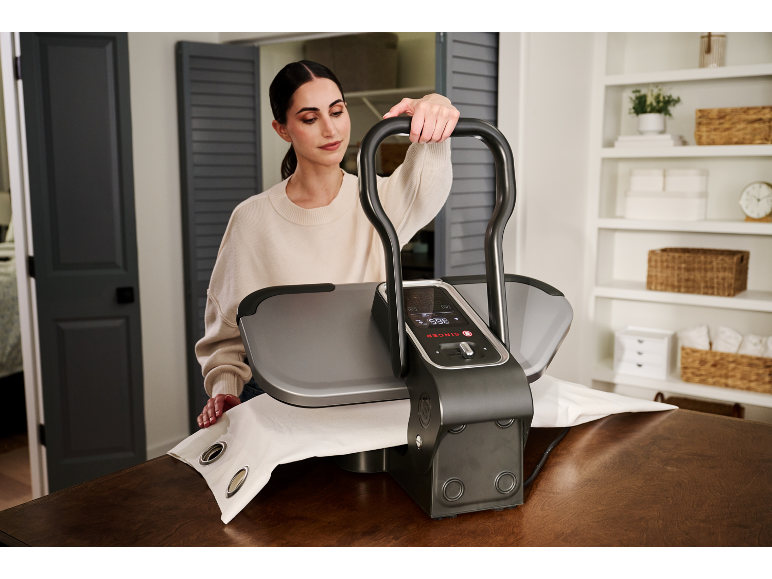 Femme utilisant une presse à repasser à vapeur pour un rideau blanc sur une table en bois.