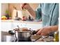 Une main ajoutant des herbes fraîches à une casserole sur une plaque à induction.