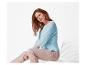 Une femme en pull bleu clair et pantalon beige est assise sur une chaise blanche.