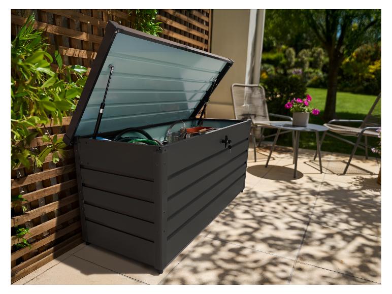 Coffre de rangement extérieur gris foncé avec couvercle ouvert, rempli d'outils de jardin, sur une terrasse.