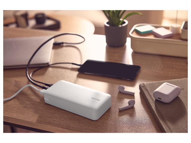 Batterie externe chargeant un téléphone et un ordinateur portable, avec des écouteurs sans fil sur un bureau.