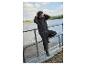 Homme en tenue imperméable noire, appuyé sur une balustrade au bord de l'eau.