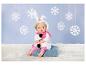 Poupée en tenue de bonhomme de neige avec écharpe rose, assise sur une couverture bleue parmi les flocons.