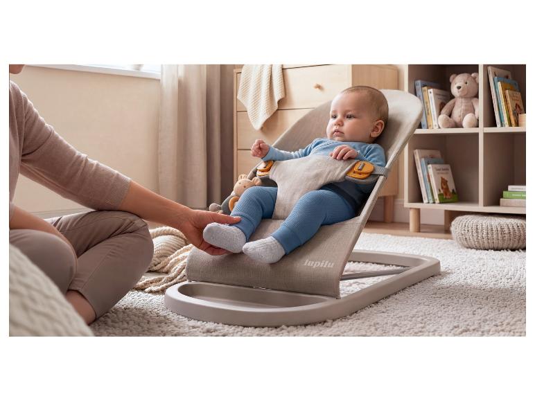 Bébé dans un transat, avec la main d'un adulte touchant le pied du bébé, sur un tapis moelleux.