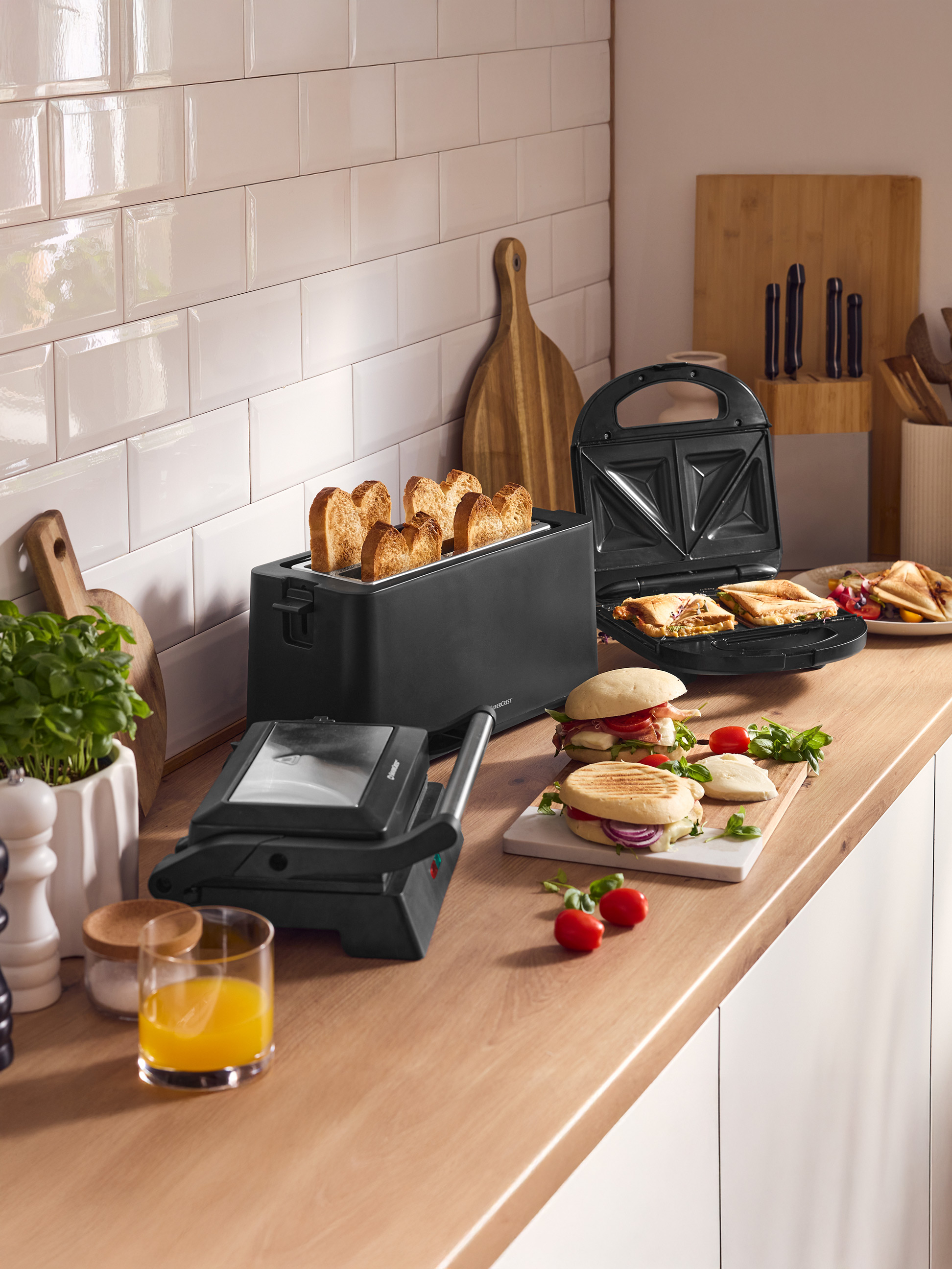 Comptoir de cuisine avec grille-pain, appareil à sandwichs et presse-grill, sandwichs préparés et jus.