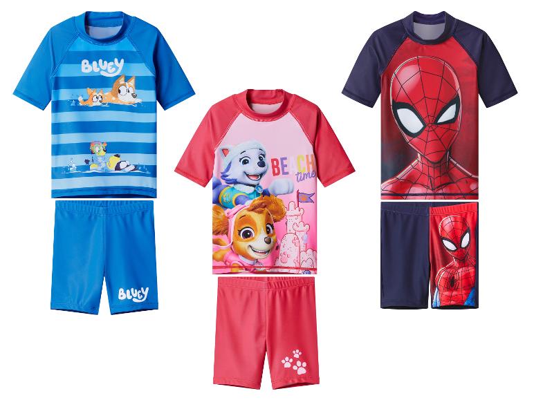 Trois ensembles de maillots de bain pour enfants: bleu avec des chiens de dessin animé, rose avec des chiots de dessin animé et rouge/bleu marine avec un super-héros.
