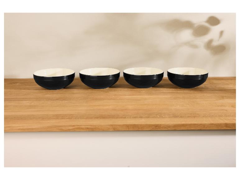 Quatre bols noirs sur une table en bois clair, avec des ombres de feuilles sur le mur.