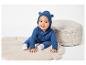 Un bébé dans une combinaison bleue est assis sur un tapis de jeu beige.