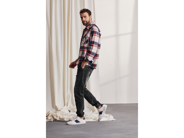Homme en chemise à carreaux, jean foncé et baskets blanches à rayures bleues.