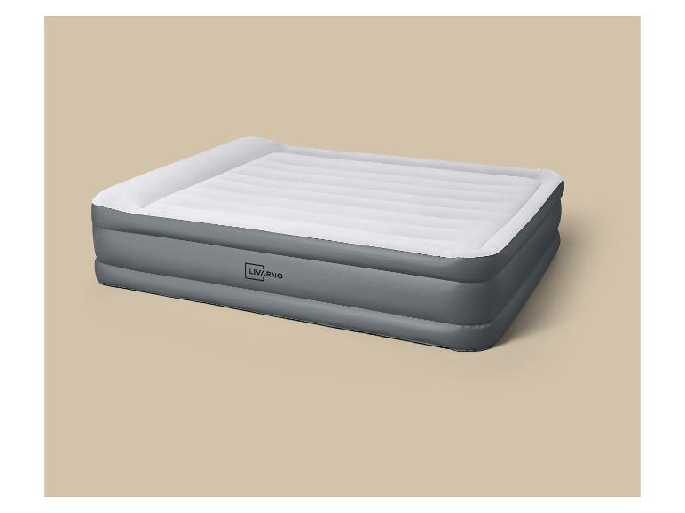 Matelas gonflable gris et blanc avec oreiller intégré sur fond beige.