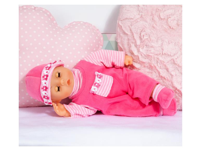 Poupée bébé rose avec bonnet et barboteuse, allongée sur une couverture douce.