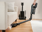 Aspirateur balai se pliant sous le canapé, à côté de la station de charge.