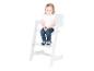Petite fille en t-shirt blanc et jean assise sur une chaise haute en bois blanc