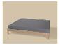 Lit en bois avec matelas gris sur fond beige.
