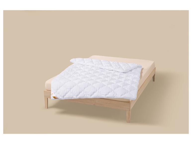 Couette blanche sur un lit en bois clair sur fond beige.