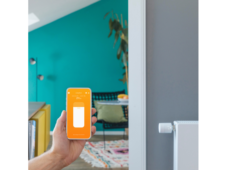 Une main tient un smartphone avec une application de contrôle de thermostats intelligents.