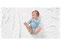 Un bébé dans un body bleu clair allongé sur une couverture blanche en tricot.