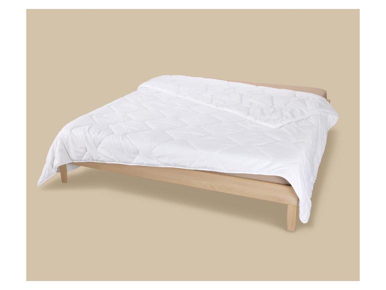 Couette blanche matelassée sur un lit en bois avec des draps beiges.
