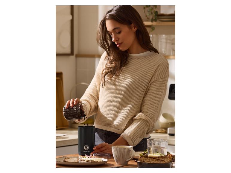 Femme versant des grains de café dans un moulin à café SilverCrest sur un comptoir de cuisine.