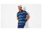 Homme en polo rayé bleu et casquette beige, appuyé contre un mur blanc.