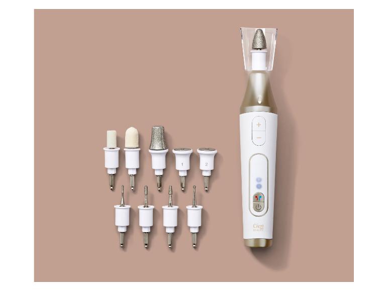 Appareil électrique de manucure/pédicure avec divers embouts, disposé sur un fond beige.