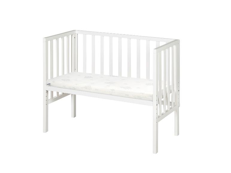 Lit bébé blanc avec matelas sur fond blanc.