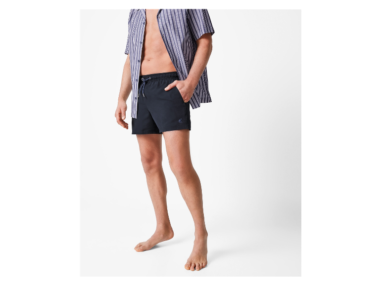 Un homme en chemise rayée et short de bain noir.