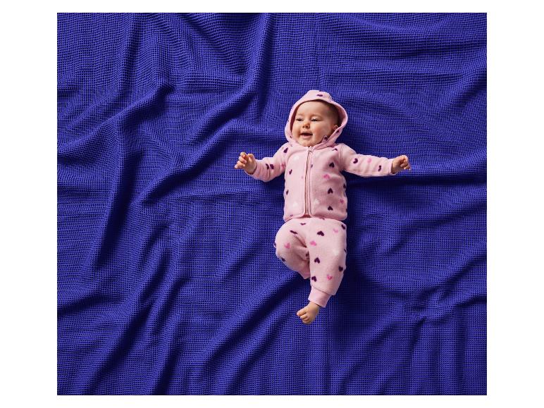 Bébé heureux en combinaison rose à cœurs, allongé sur une couverture bleue