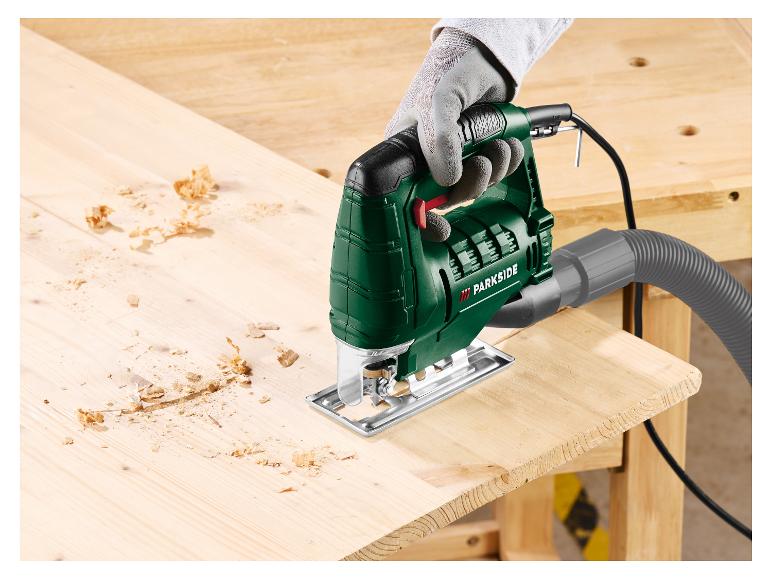 Scie sauteuse Parkside verte coupant une planche de bois avec des copeaux.