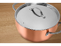 Casserole en cuivre avec couvercle en acier inoxydable sur une surface en bois.