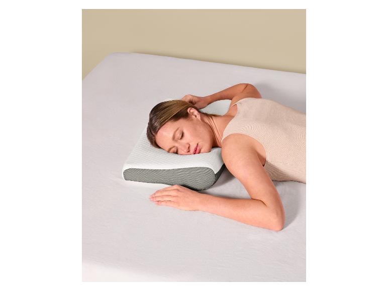 Femme dormant sur un oreiller ergonomique blanc et gris sur un lit aux draps blancs.