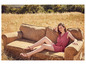 Une femme en robe rose et sandales est assise sur un vieux canapé dans un champ d'herbe.