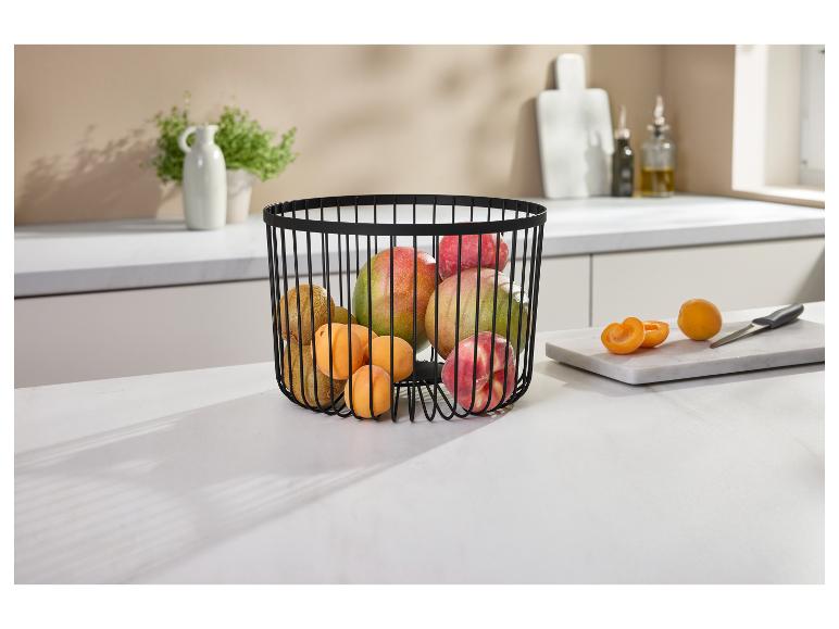 Corbeille à fruits en fil noir remplie de mangues, kiwis, pêches et abricots sur un comptoir de cuisine.