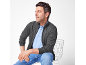 Homme en cardigan gris zippé, polo bleu clair et jean bleu, assis sur une chaise.