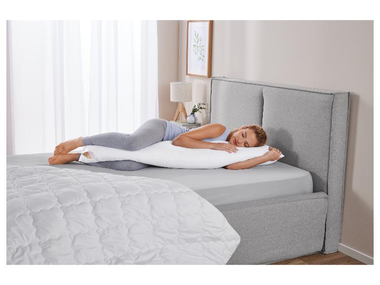 Une femme dort paisiblement sur un lit avec un oreiller de grossesse.