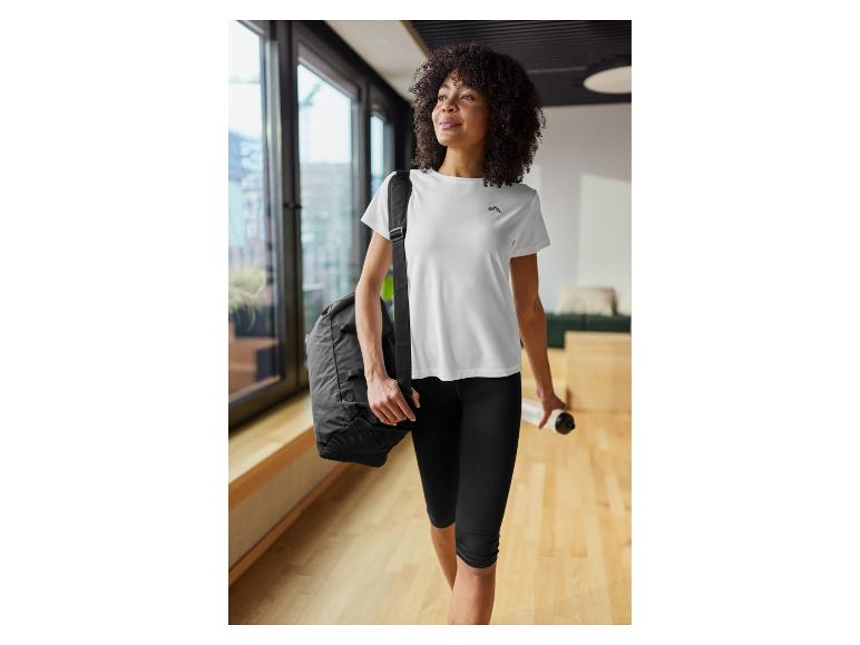 Femme en t-shirt de sport blanc et legging noir, portant un sac de sport et une bouteille d'eau.