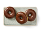 Trois beignets glacés au chocolat sur une assiette rectangulaire texturée bleu clair.