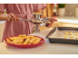 Femme utilisant une presse à biscuits pour faire des biscuits, avec une plaque de cuisson et une assiette de biscuits.