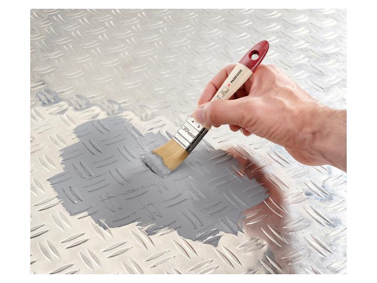 Une main appliquant de la peinture grise sur une surface métallique avec un pinceau Parkside.