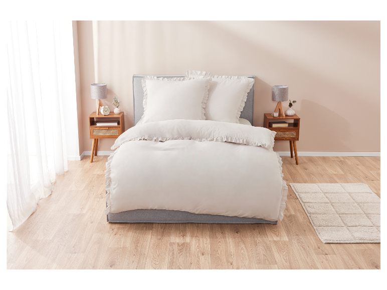 Draps beiges clairs avec volants sur un lit gris.