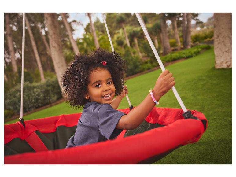 Fille souriante dans une balançoire de jardin avec un siège rouge.