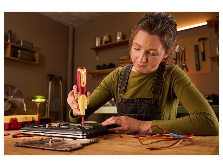 Femme utilisant un tournevis Parkside pour réparer un ordinateur portable sur un bureau en bois.