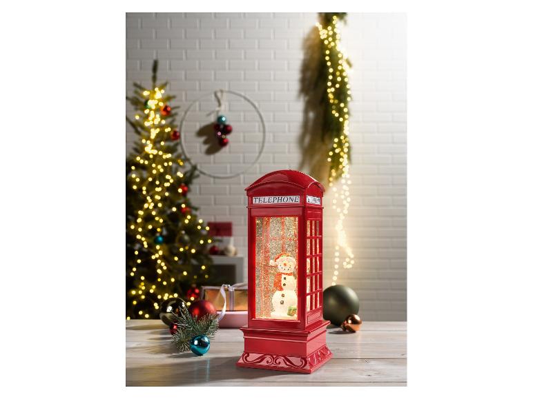 Un globe de neige rouge en forme de cabine téléphonique avec un bonhomme de neige, entouré de décorations de Noël.