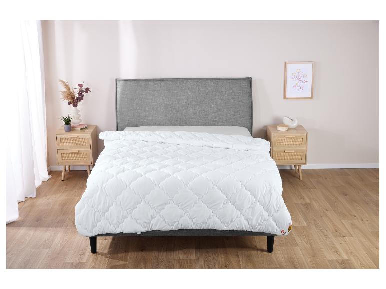Une couette blanche avec un motif en losange sur un lit gris dans une chambre.