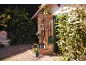 Outils de jardinage suspendus à une porte en bois, avec une pelle et un râteau au premier plan.