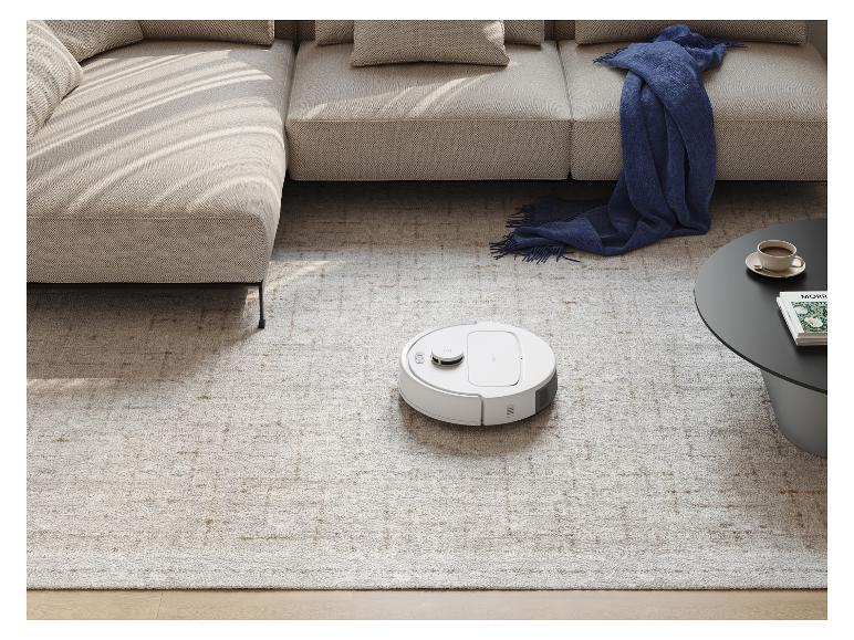 Aspirateur robot sur un tapis clair dans un salon moderne avec un canapé et une table basse.