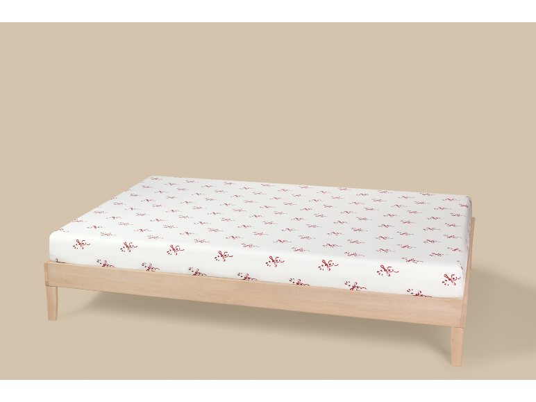 Drap-housse blanc à motifs de nœuds rouges sur un lit en bois.