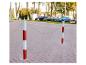 Deux poteaux rouges et blancs avec une chaîne sur un trottoir pavé, avec des voitures en arrière-plan.